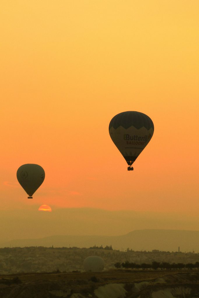 Scenic view of hot air balloons over Cappadocia at sunset, showcasing a vibrant orange sky.